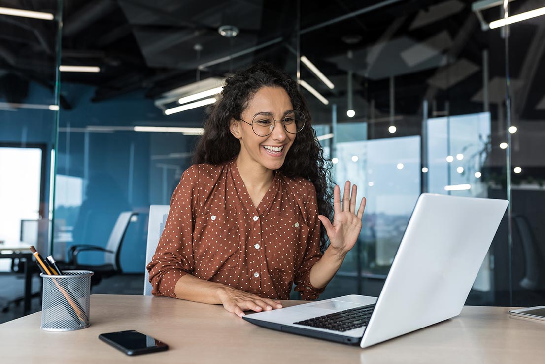 A smiling woman greeting others in a meeting.