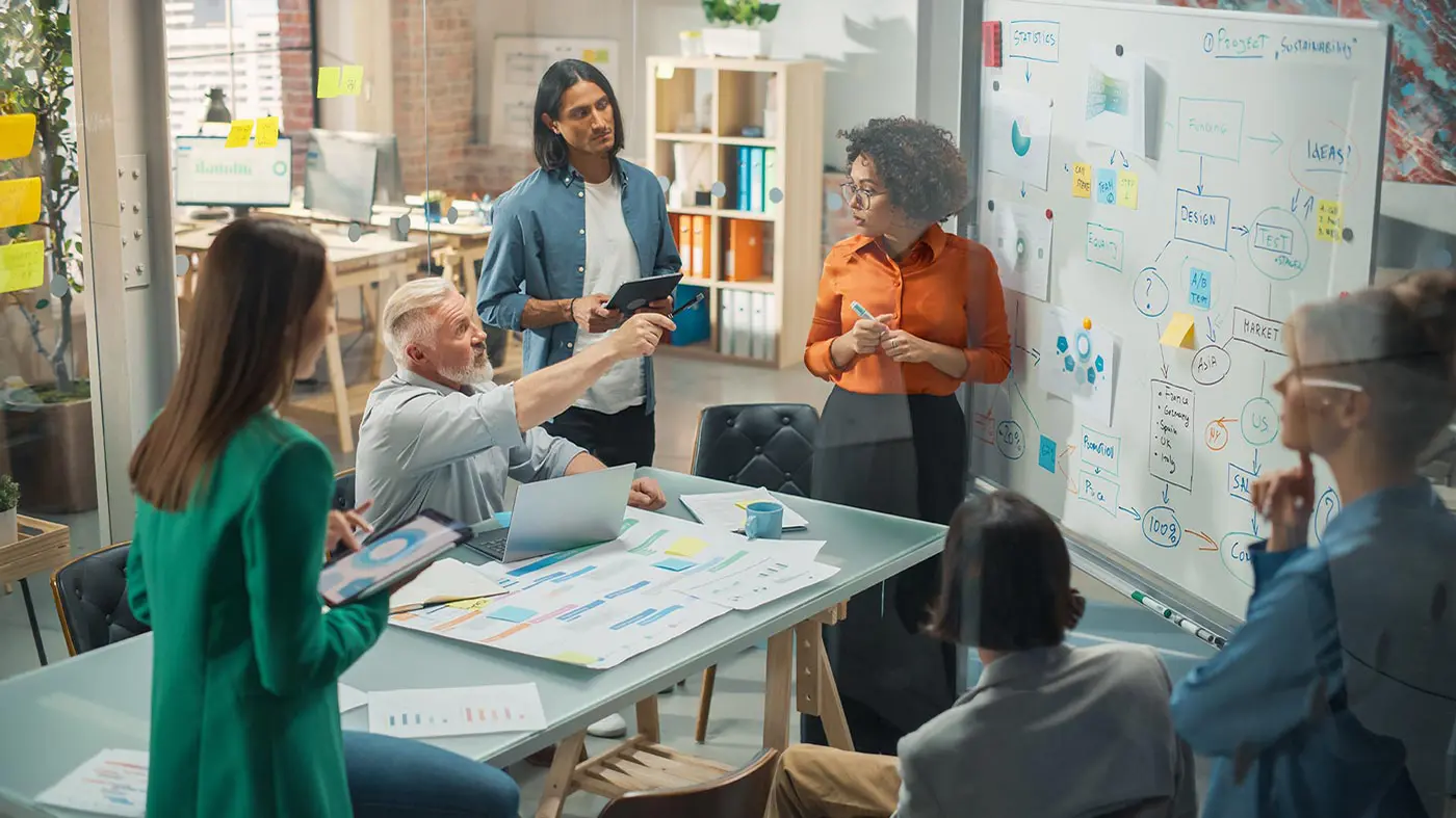 A team gathered around a whiteboard covered in diagrams and sticky notes, mid-discussion